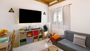 Ein Wohnzimmer mit Flachbildfernseher, Holzbalken, einer Couch, einem Couchtisch und einem Fenster mit Vorhängen.