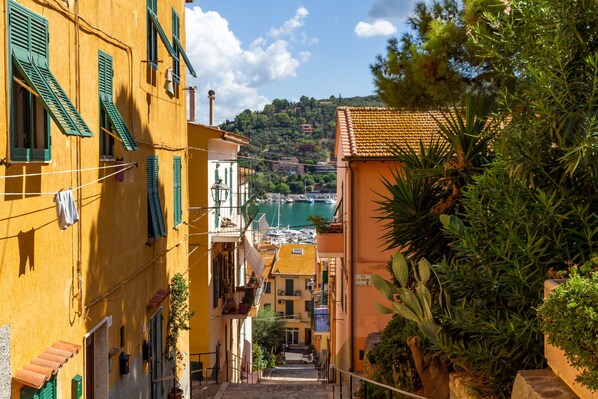 A narrow street with buildings on either side, a clear sky, and a view of a marina in the distance.