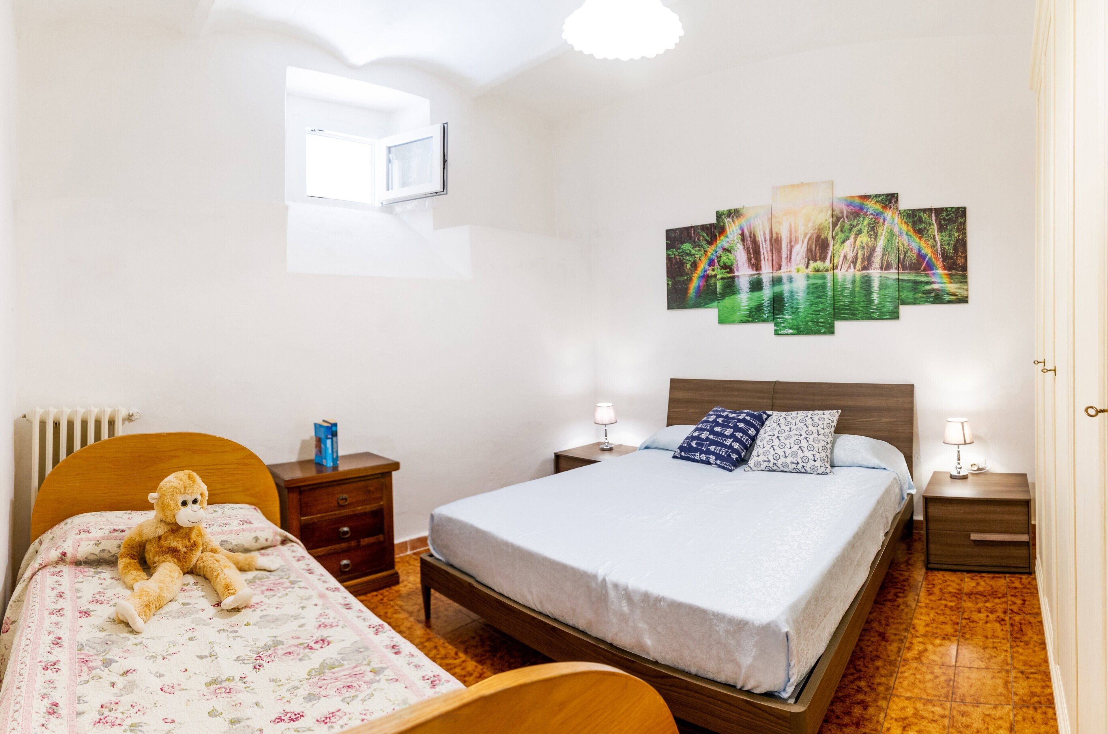 Une chambre à coucher comprenant un lit, une table de chevet, une chaise, un ours en peluche, un radiateur et un tableau accroché au mur.