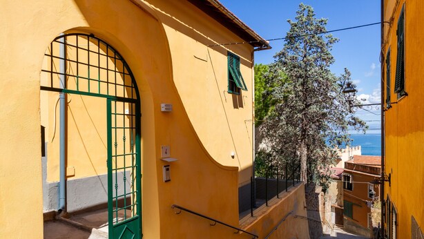 Una calle estrecha con un edificio amarillo, un portón verde y una escalera que sube a un nivel superior.