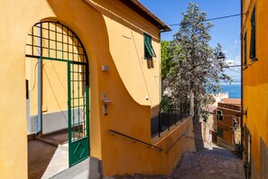 Une rue étroite avec un immeuble jaune, un portail vert et un escalier menant à un niveau supérieur.