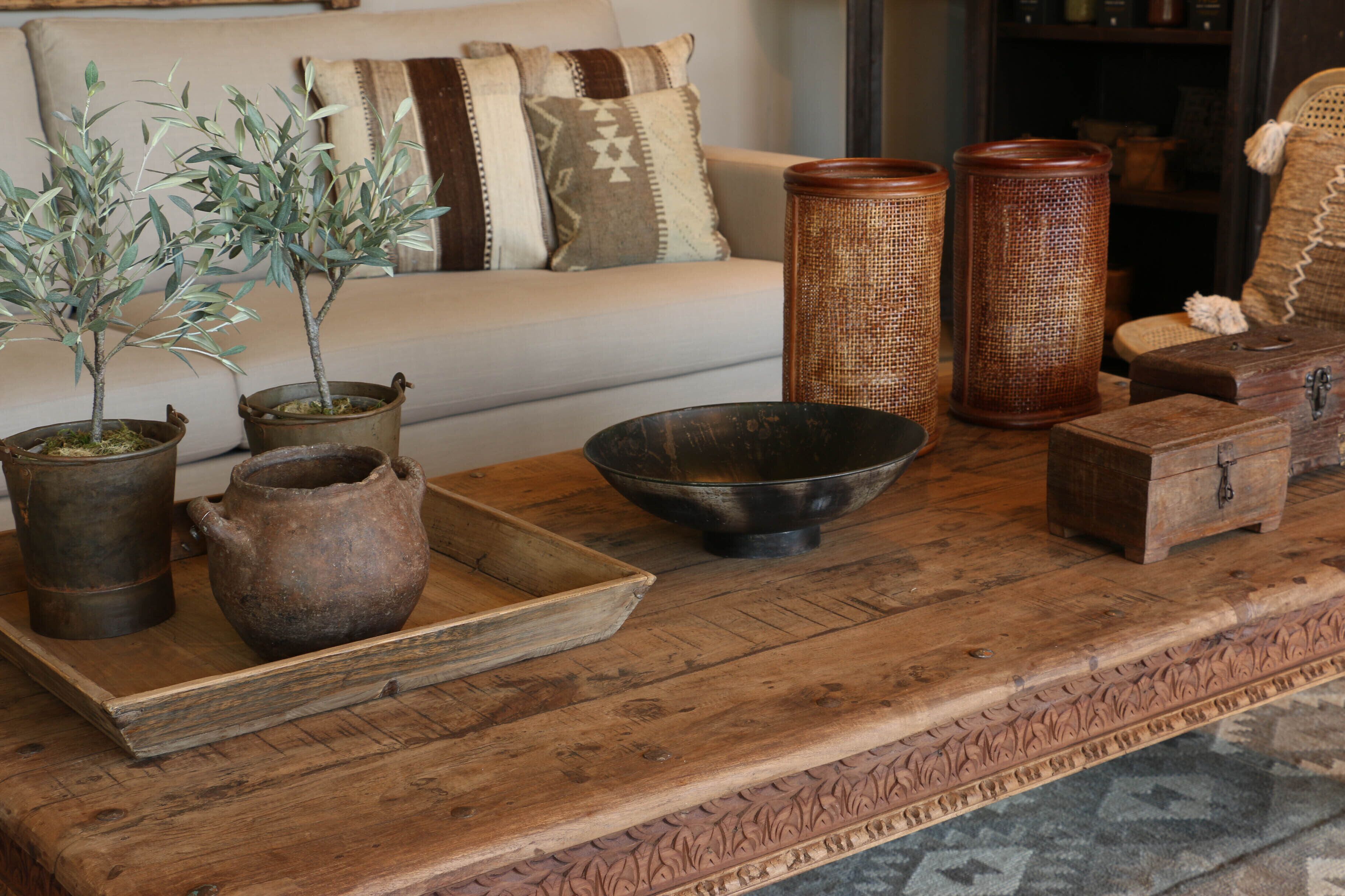 Une table en bois avec un plateau, deux plantes en pot, un bol en métal et une petite boîte en bois.