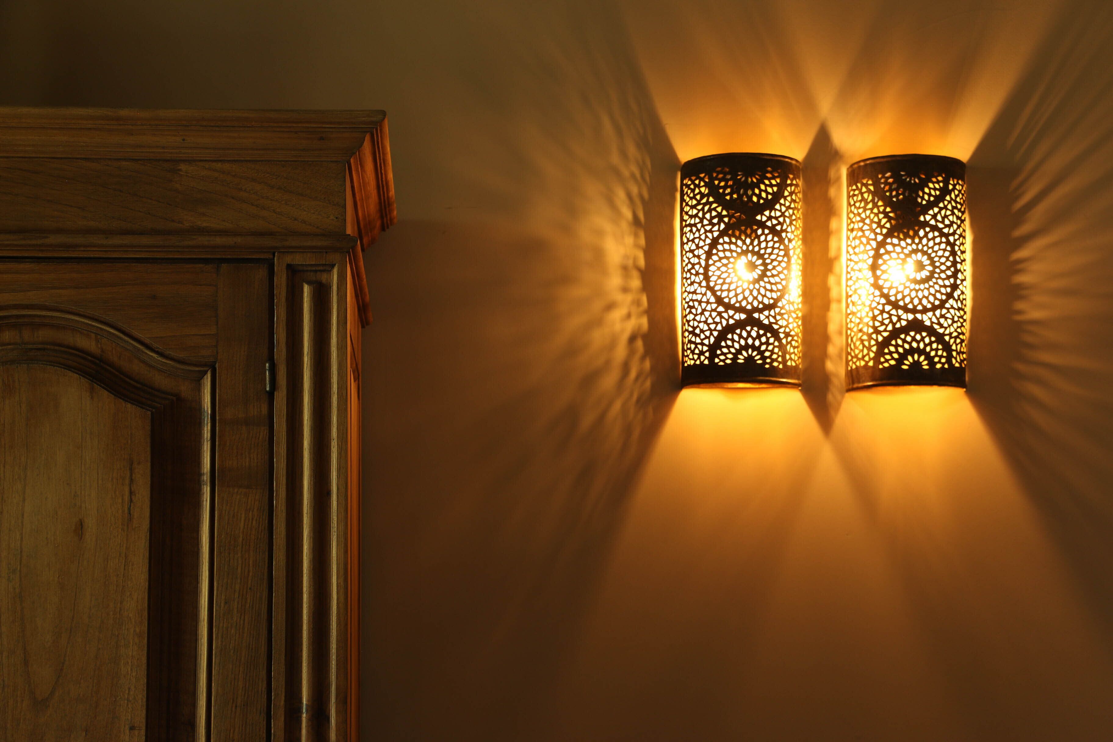 Two wall-mounted lamps with intricate patterns, casting warm light on a wall.