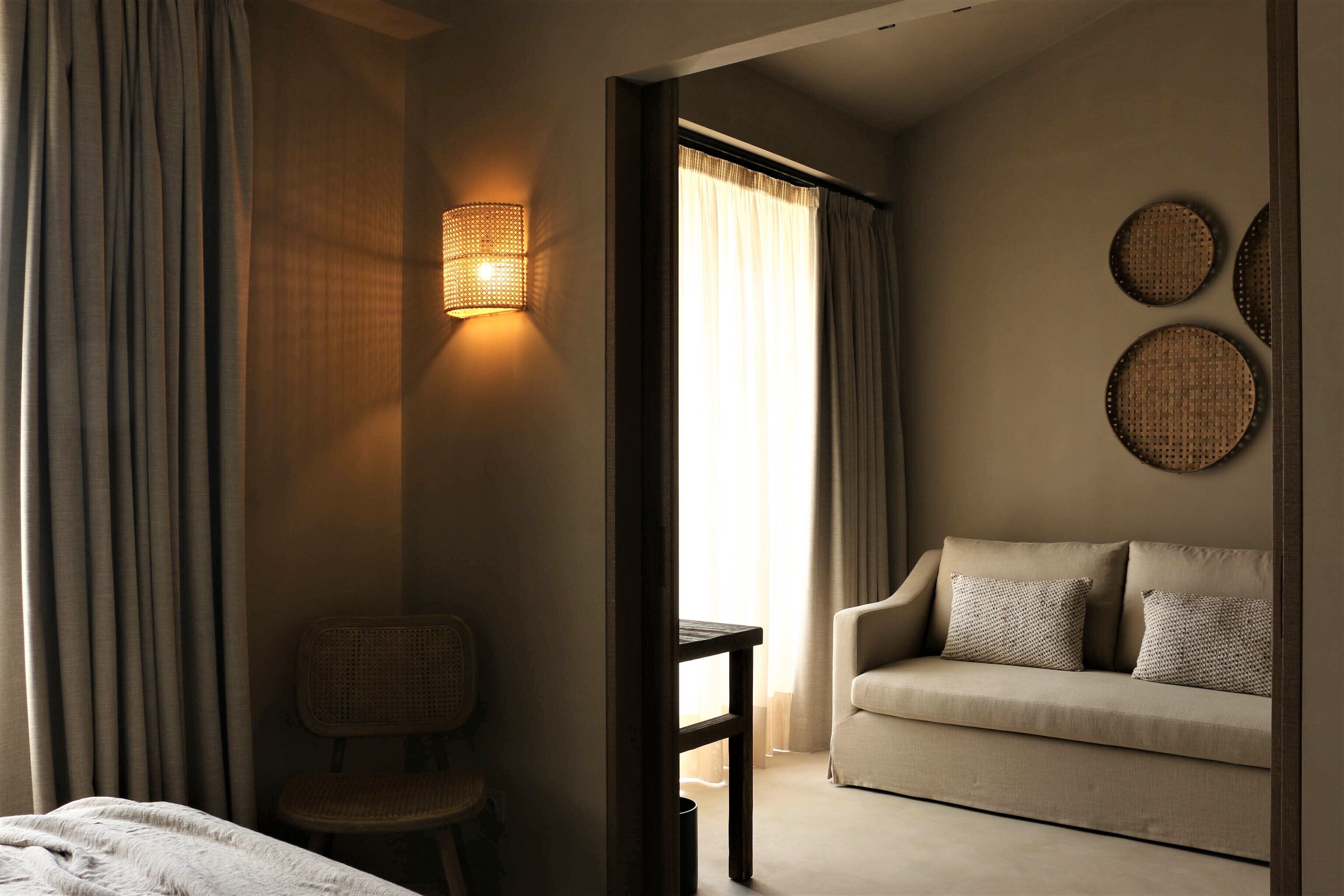 A hotel room with a bed, a sofa, a chair, a small table, and a wall-mounted lamp.