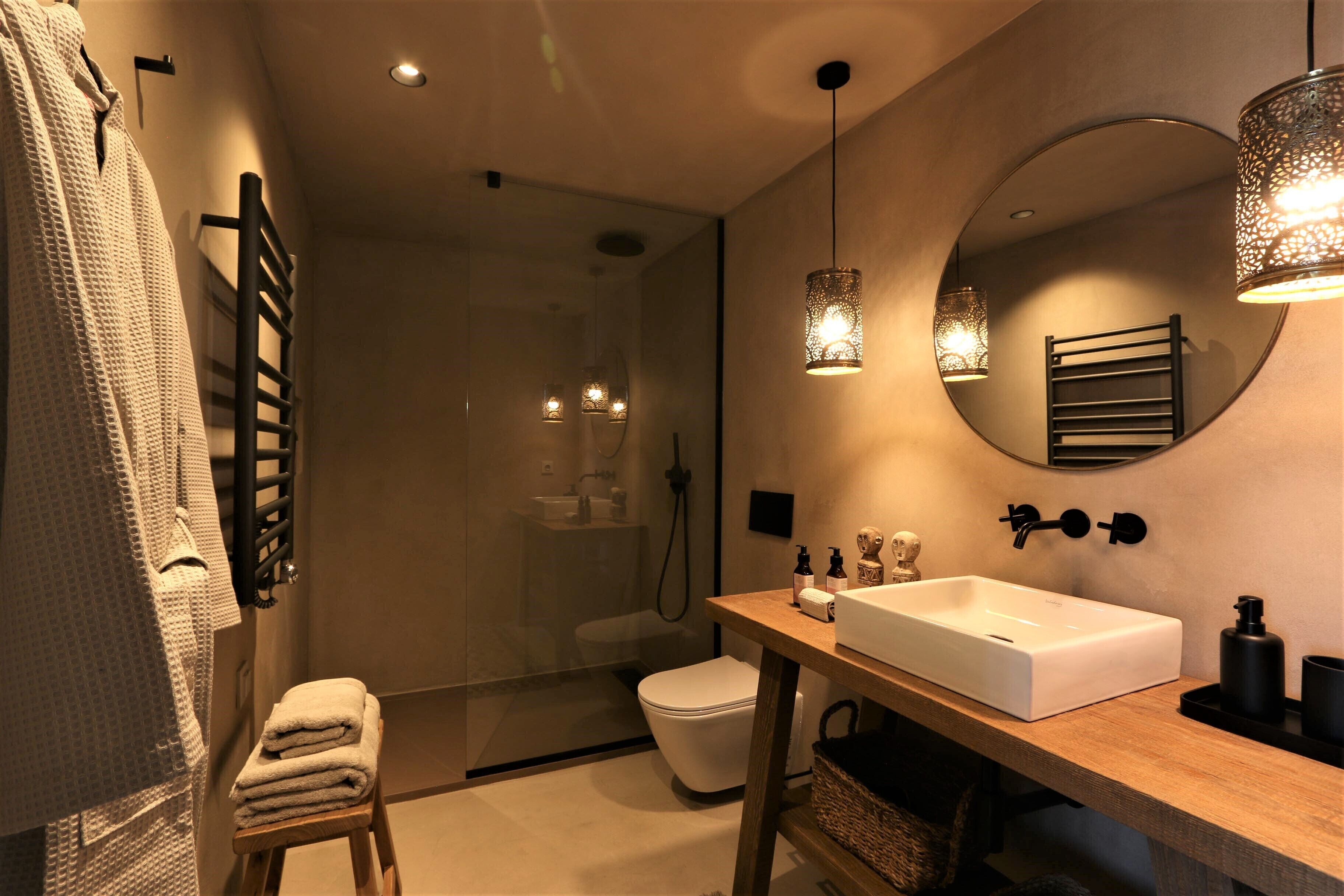 Un baño moderno con un espejo grande, un mueble de tocador de madera, un lavamanos blanco y una cabina de ducha de vidrio.