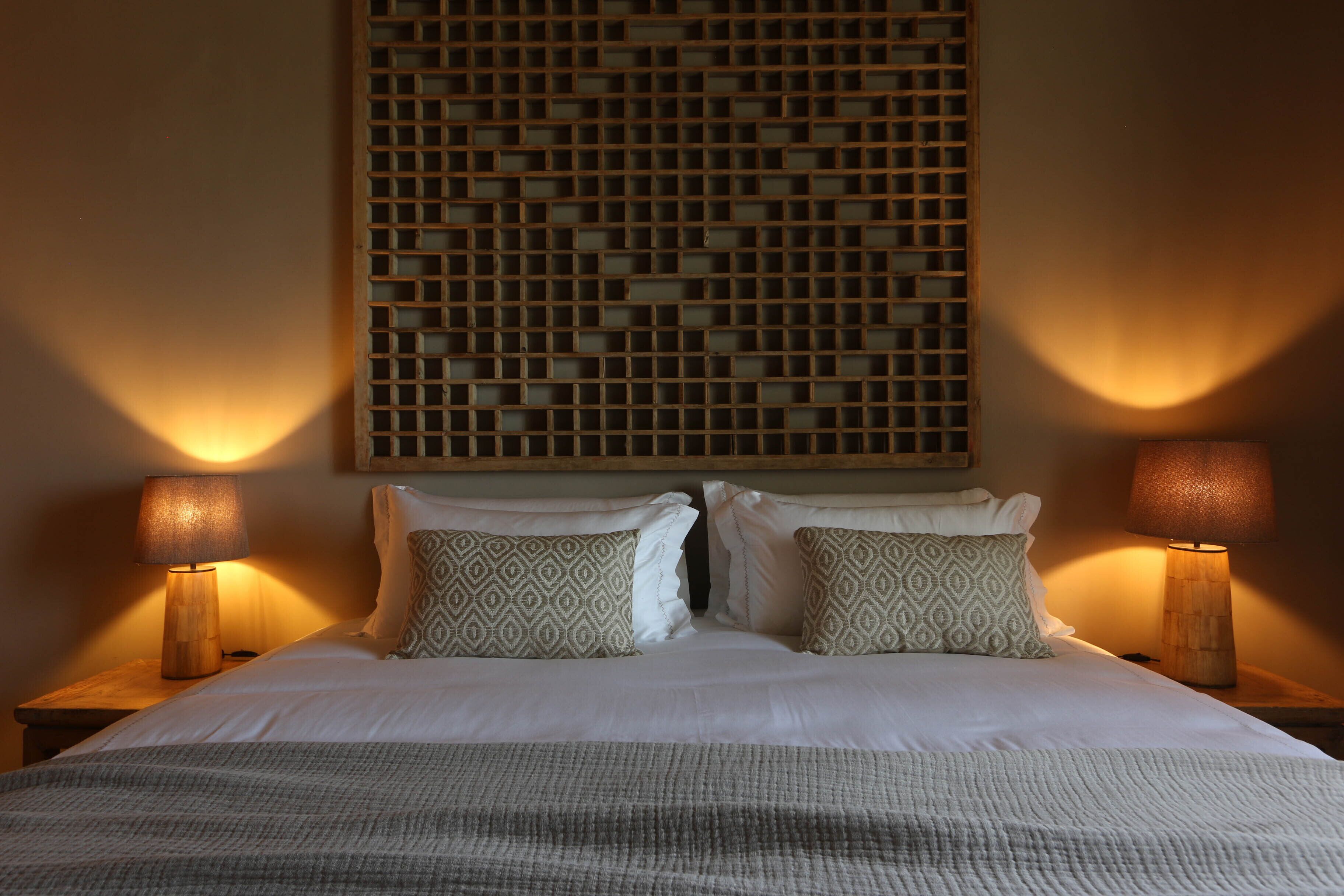 A neatly made bed with patterned pillows, two bedside lamps, and a decorative wall panel above.