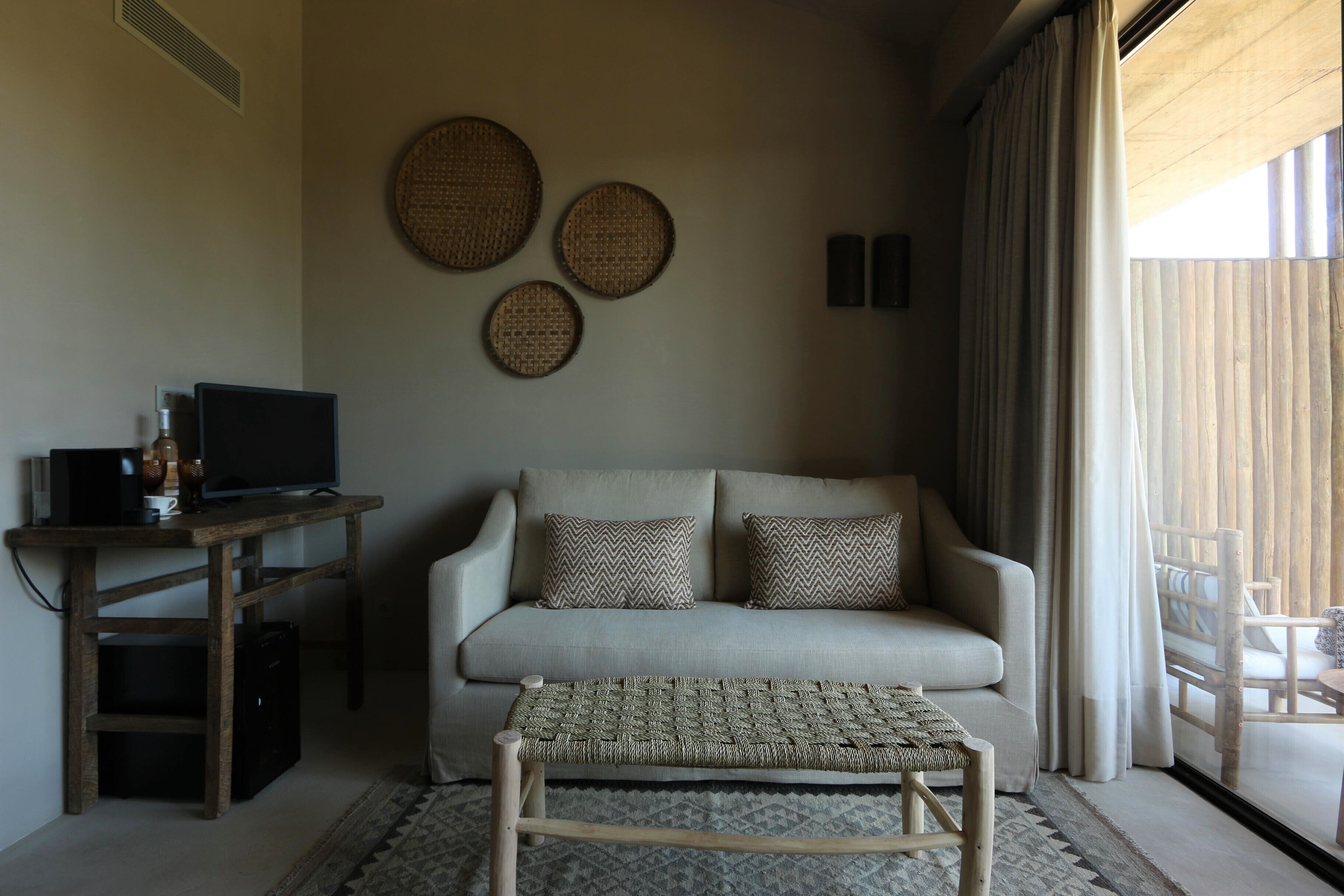 A living room with a sofa, a coffee table, a TV on a wooden stand, and three woven wall decorations.