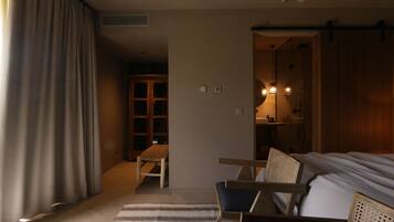 Habitación de hotel con cama, dos sillas de madera, alfombra a rayas, armario y un pequeño rincón de descanso con una silla y una mesa.
