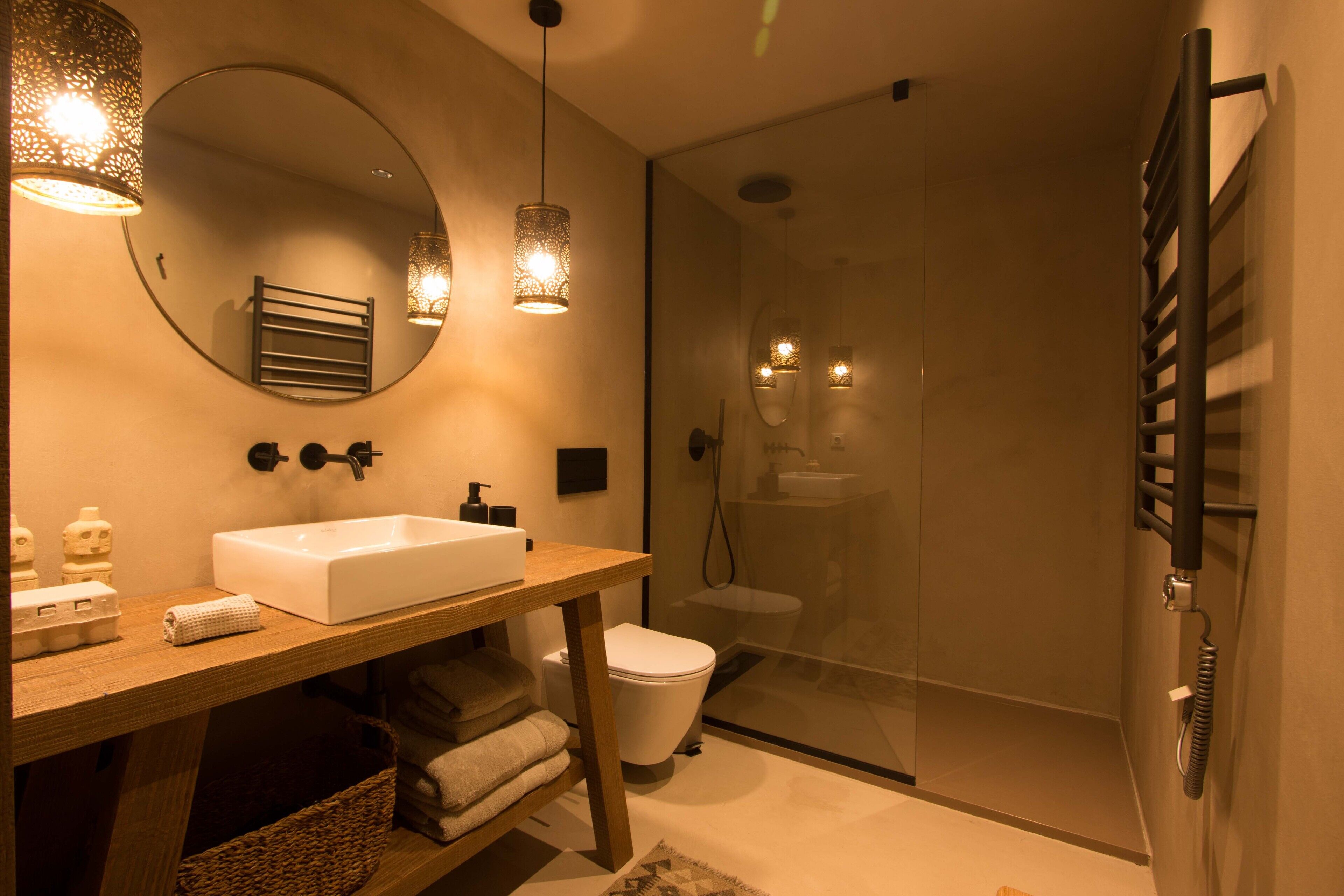 Un baño moderno con tocador de madera, un espejo grande, un lavamanos blanco y una ducha con cerramiento de vidrio.