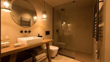 Un baño moderno con tocador de madera, un espejo grande, un lavamanos blanco y una ducha con cerramiento de vidrio.