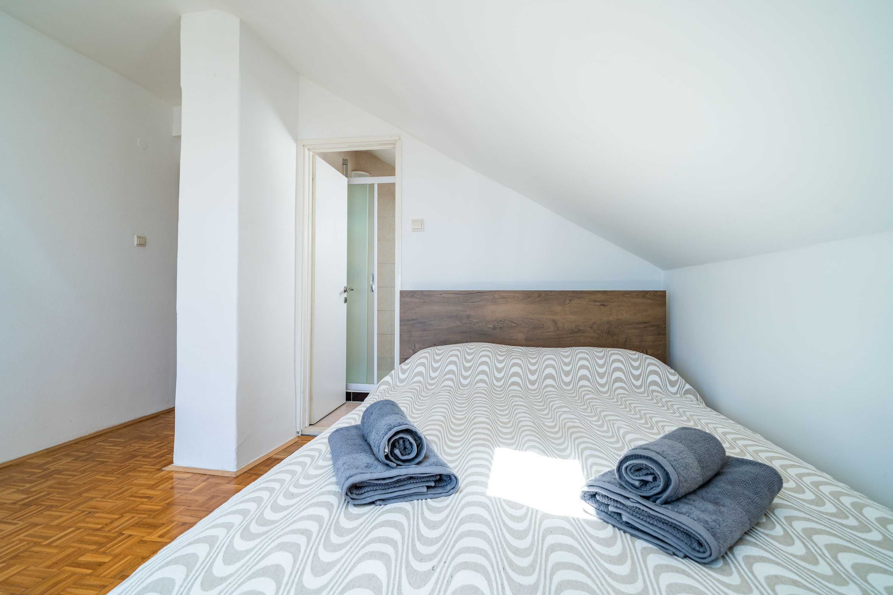 Ein Schlafzimmer mit einem Bett, zwei zusammengerollten Handtüchern, einem hölzernen Kopfteil und einer Tür zu einem Badezimmer.