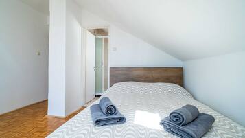Ein Schlafzimmer mit einem Bett, zwei zusammengerollten Handtüchern, einem hölzernen Kopfteil und einer Tür zu einem Badezimmer.