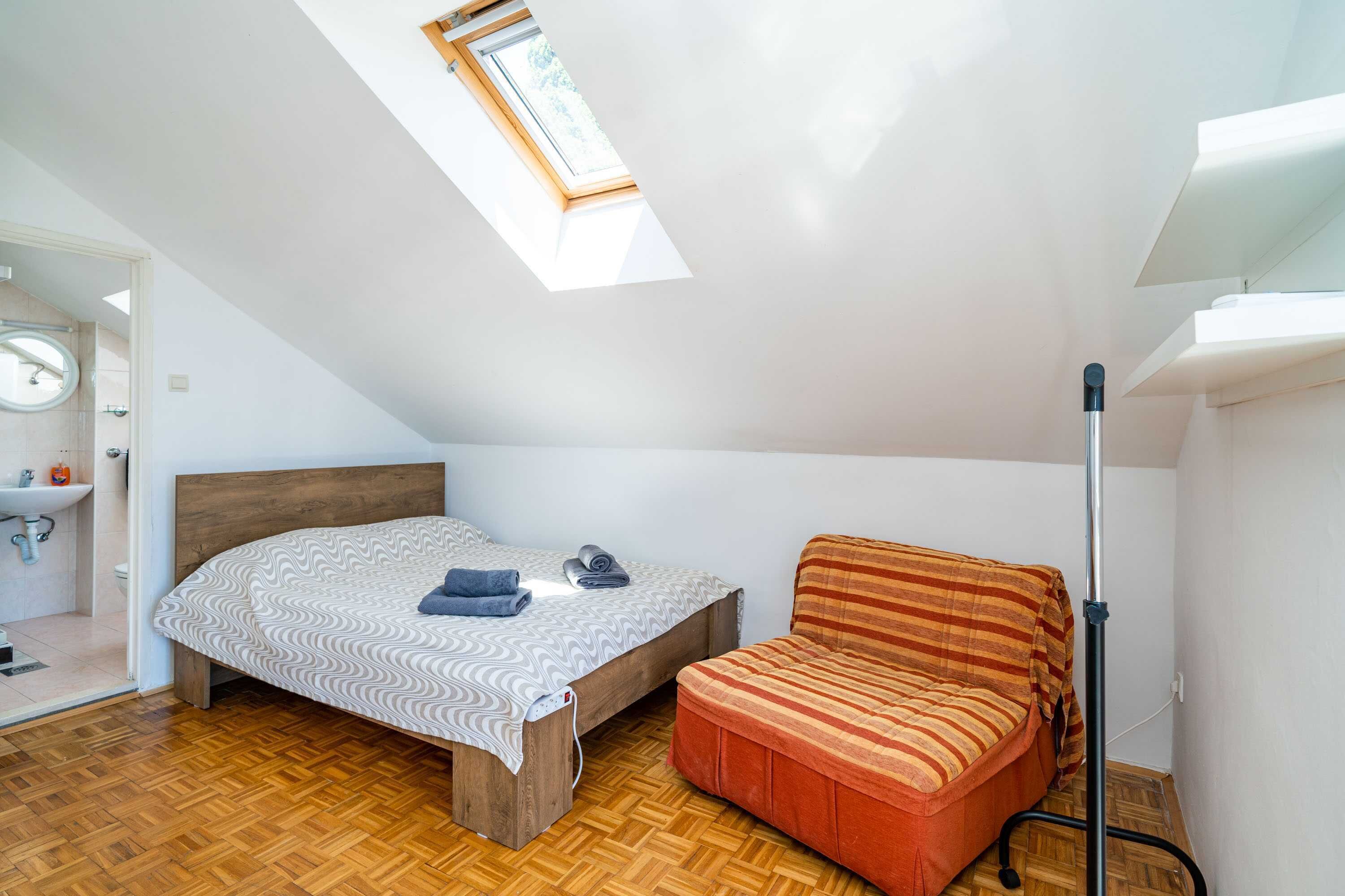 A bedroom with a bed, a sofa, a skylight, a floor lamp, and a bathroom with a sink and toilet.