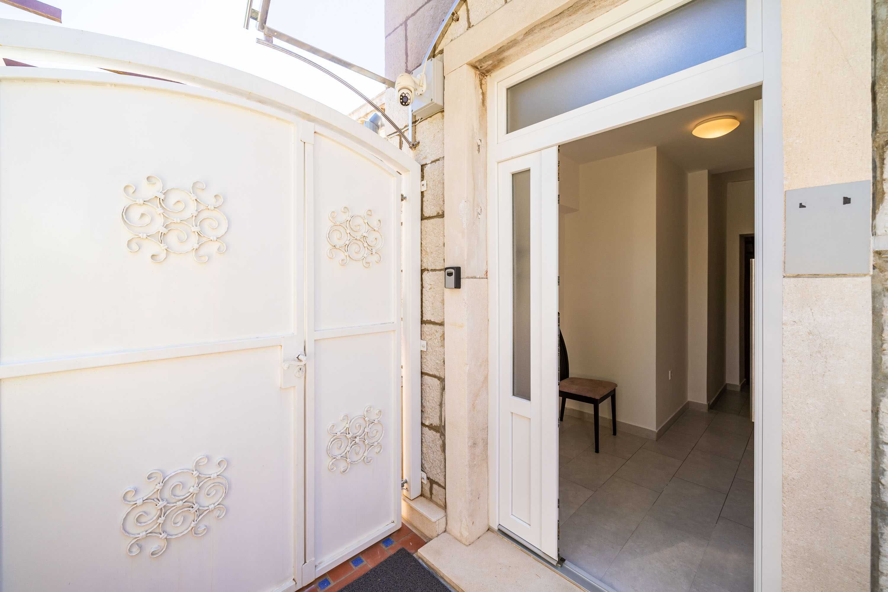 Una porta bianca con decorazioni in metallo, un muro in pietra e un pavimento piastrellato che conducono in una stanza con una panca.
