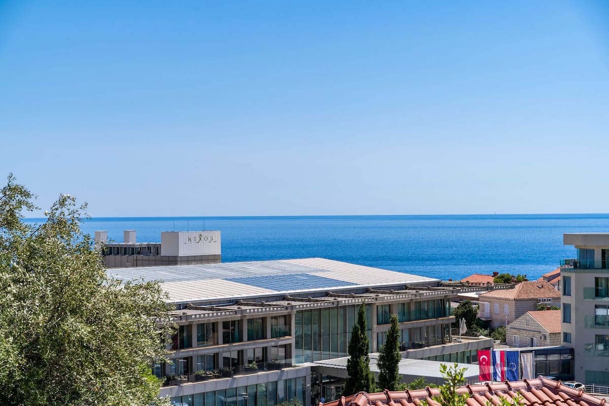 A modern hotel with a glass facade, a rooftop terrace, and views of the sea.