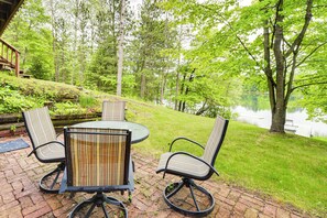 Eine Terrasse im Freien mit einem runden Tisch und vier Stühlen, umgeben von üppiger Vegetation und Blick auf einen See.