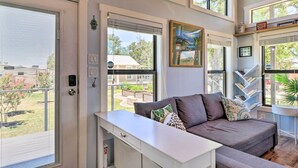 A modern living room with a grey sofa, white console table, and large windows offering views of the outdoors. - Upscale Tiny Home - Boho-Chic Austin Getaway! (Austin)