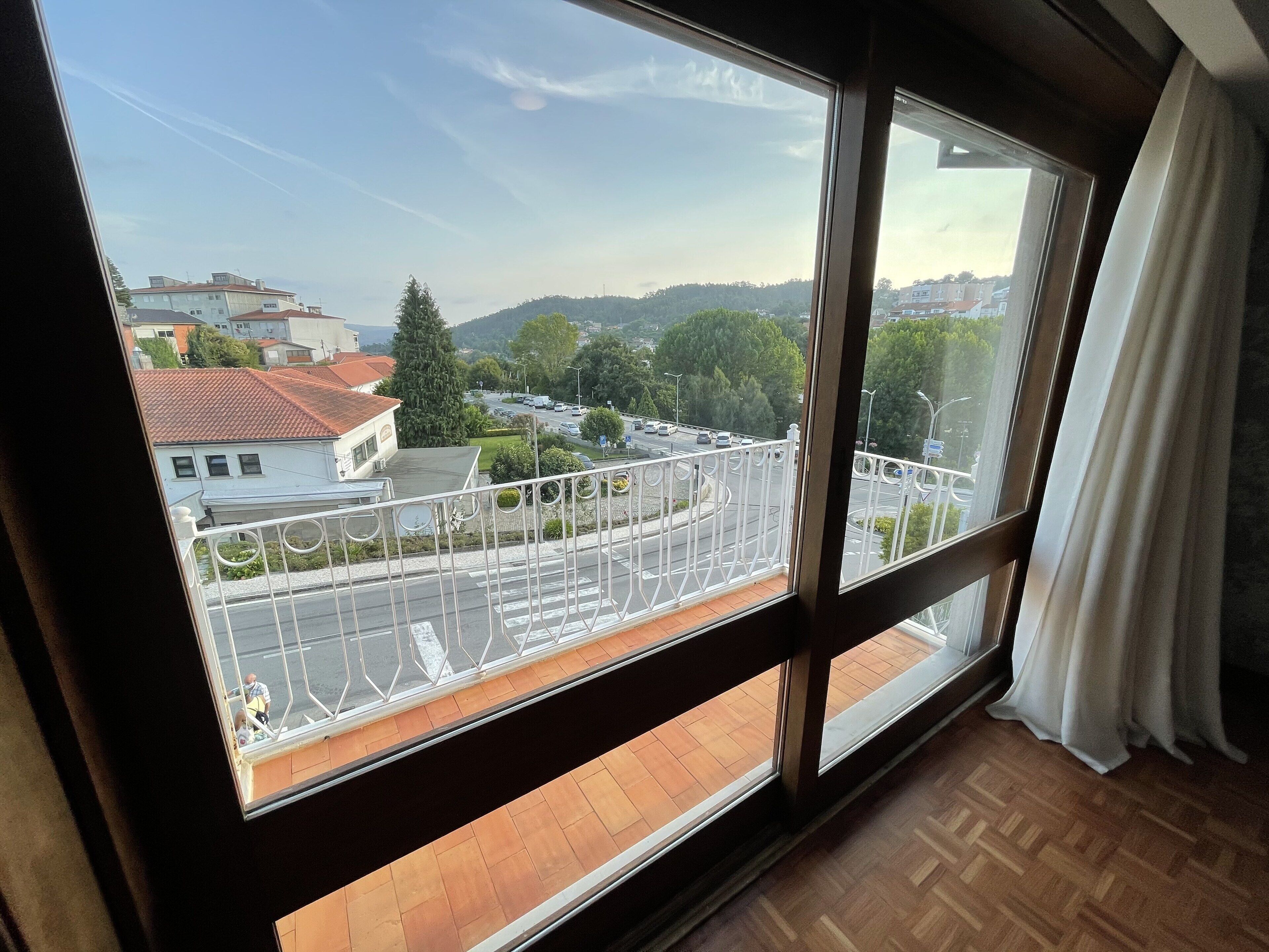 A room with a large window overlooking a road with a white fence and trees.