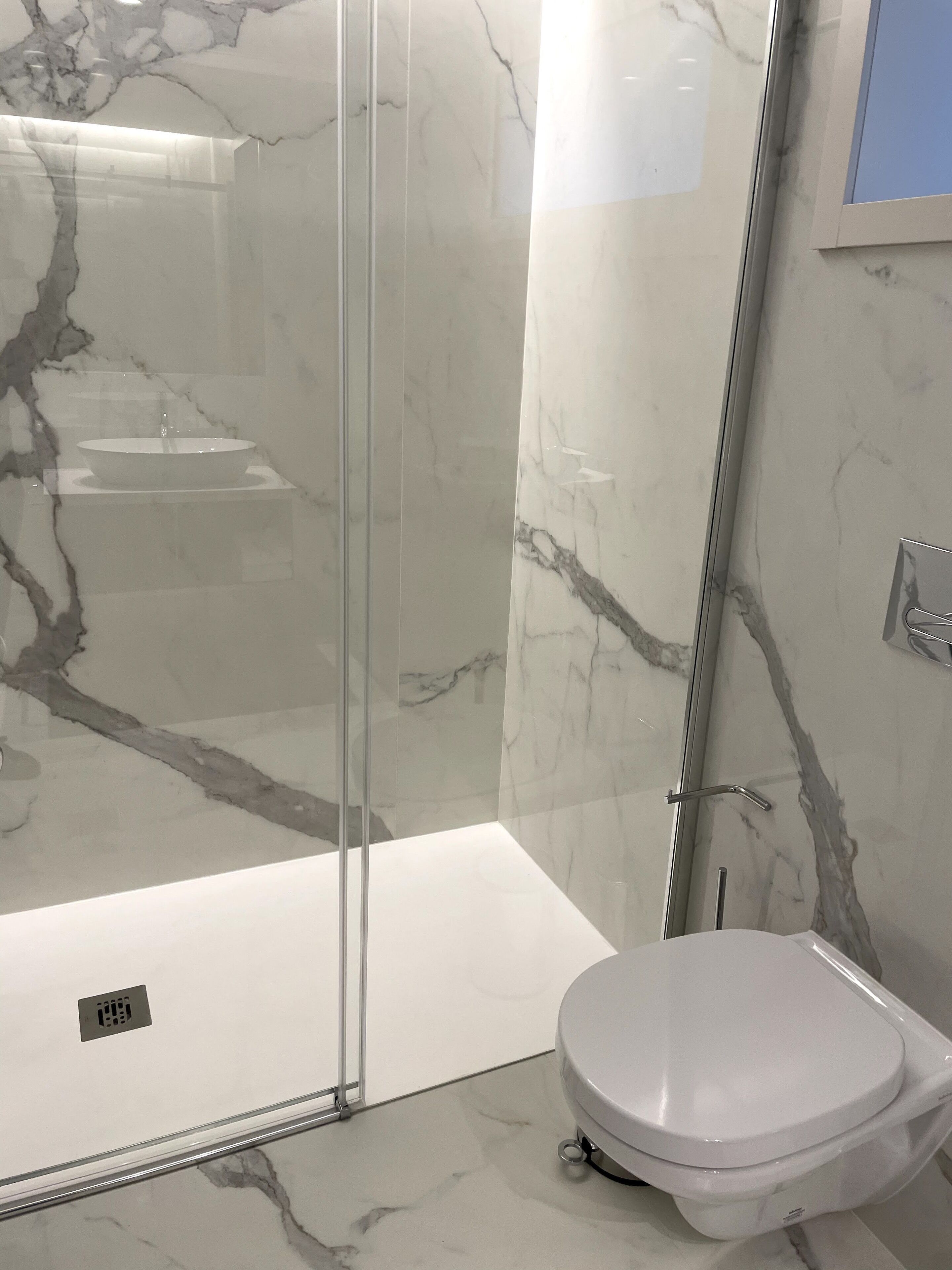 Un baño moderno con ducha de vidrio, un lavamanos blanco y un inodoro.
