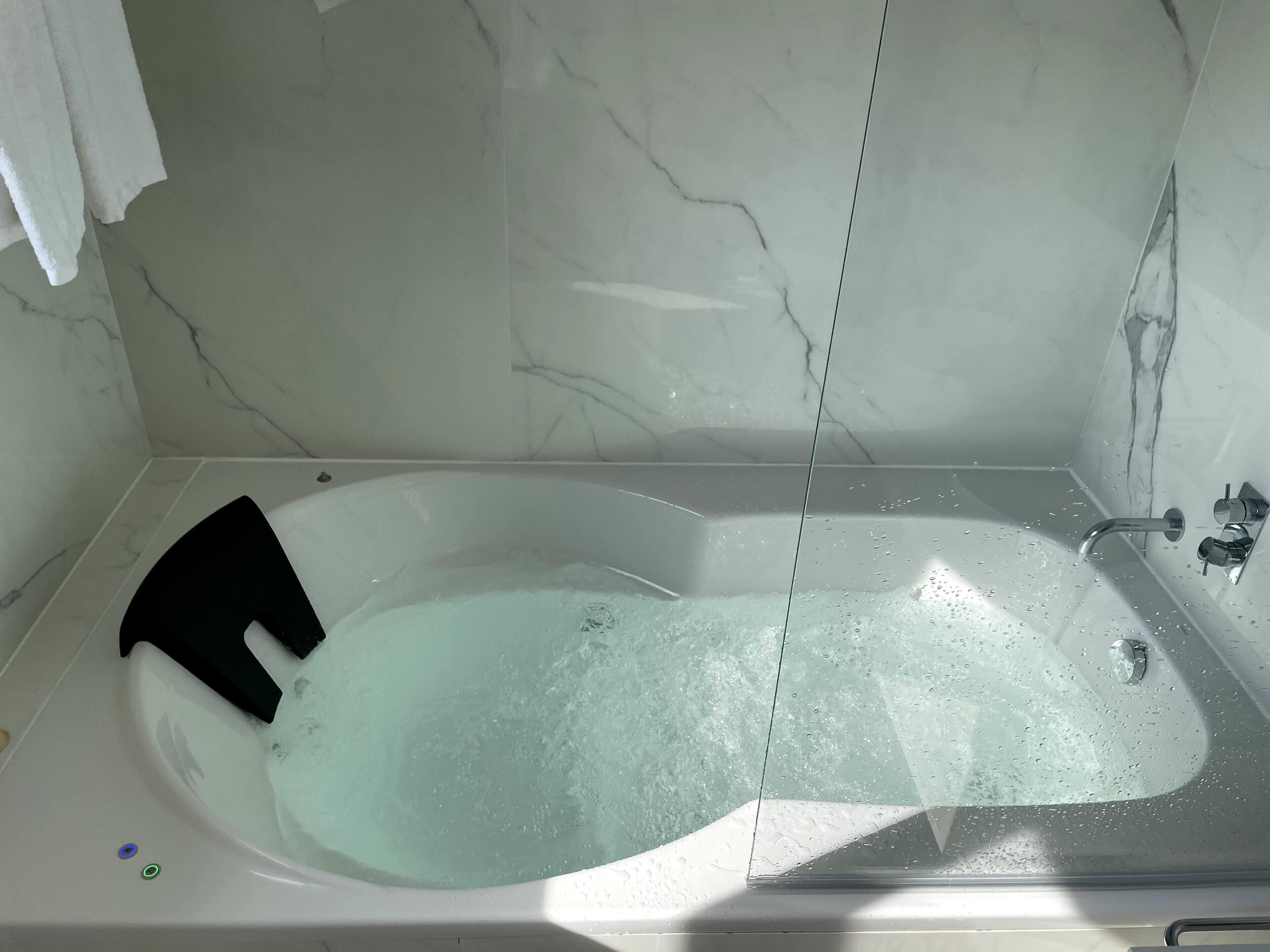 A modern bathroom with a freestanding bathtub, marble walls, and a glass shower enclosure.