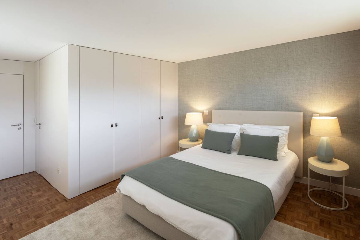 Een moderne slaapkamer met een groot bed, twee nachtkastjes met lampen, een kledingkast en een vloerbedekking.