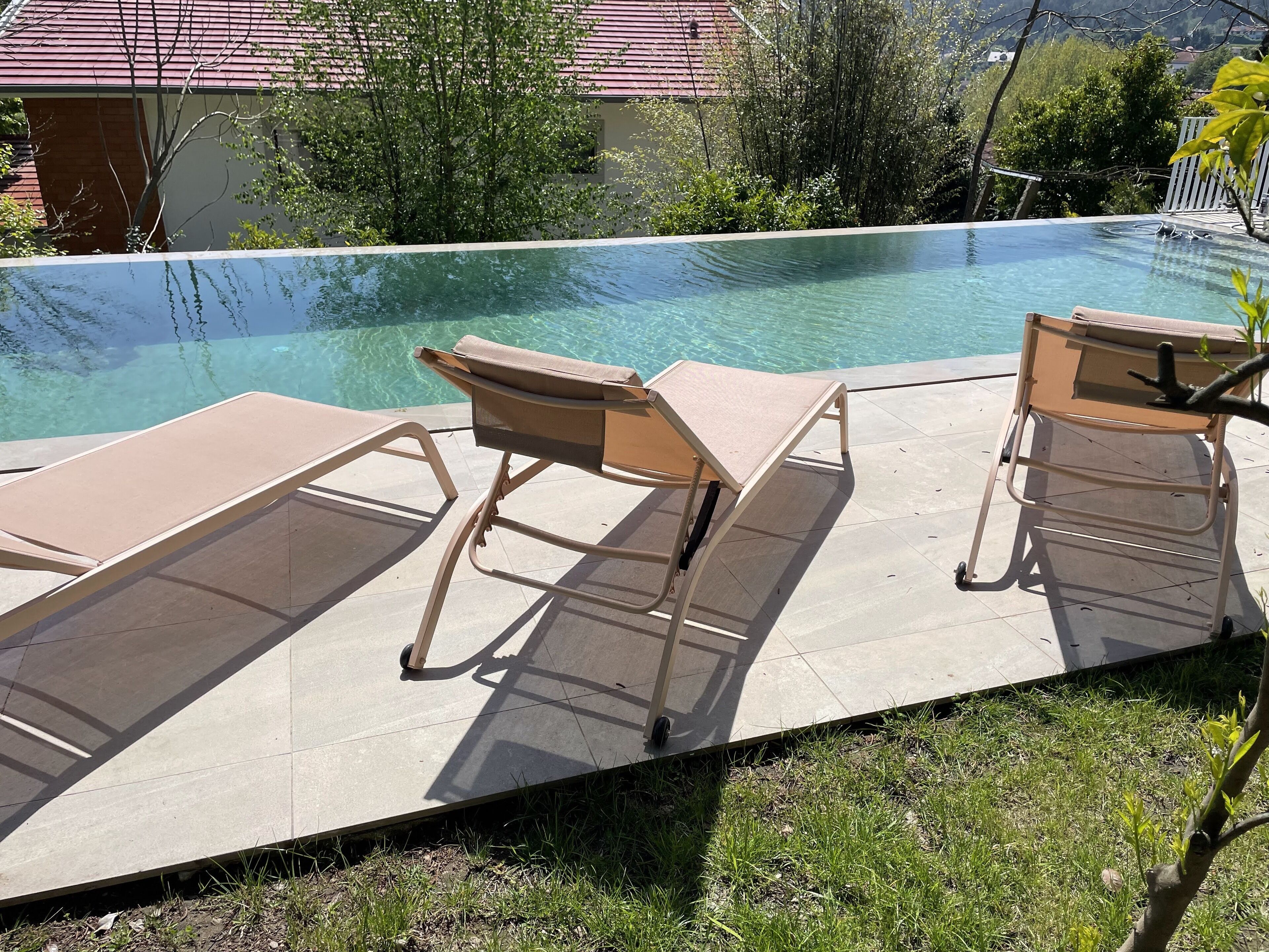 En pool med två solstolar och en kakelbeklädd terrass.