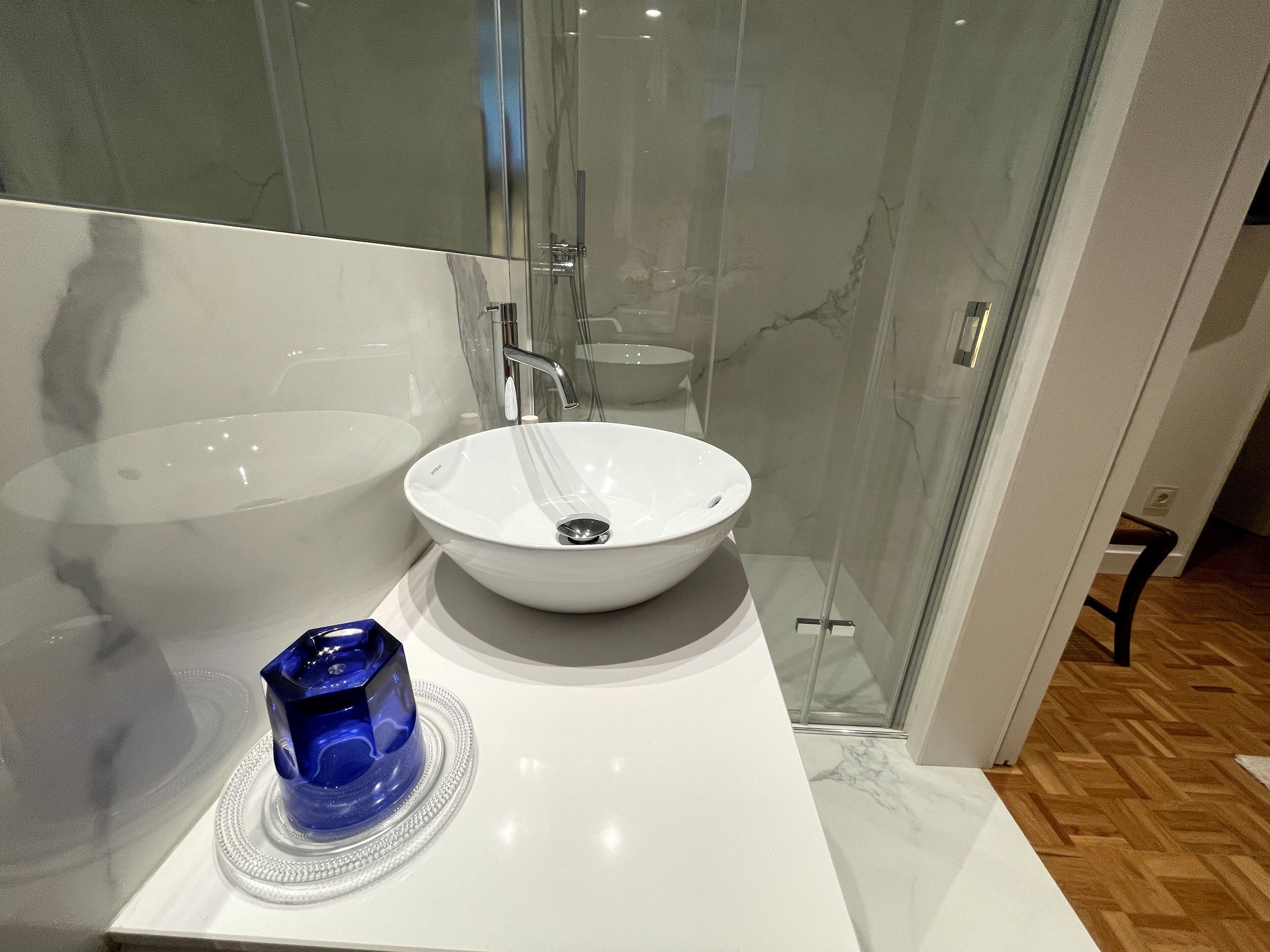 A modern bathroom with a white sink, a glass shower enclosure, and a blue decorative item on the counter.