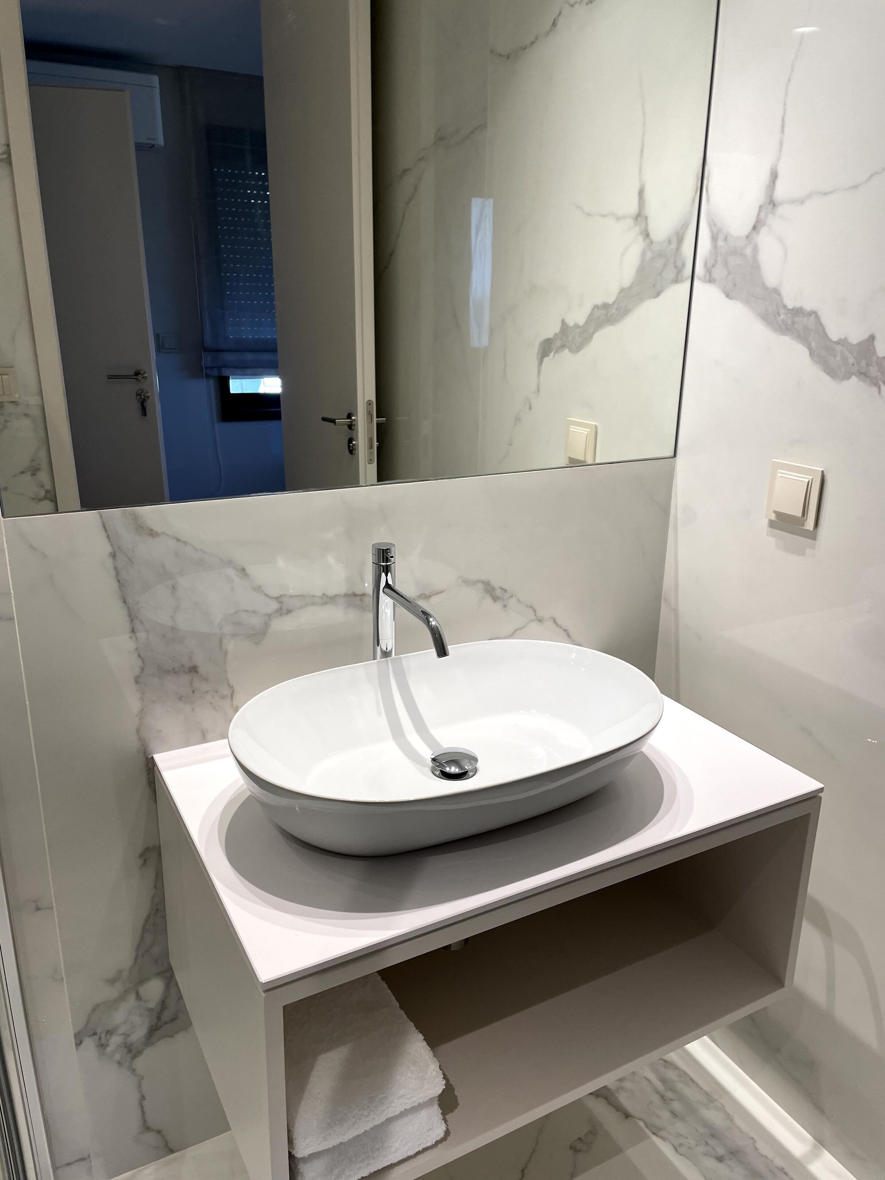 Een moderne badkamer met een marmeren wastafelmeubel, een witte wasbak en een spiegel.