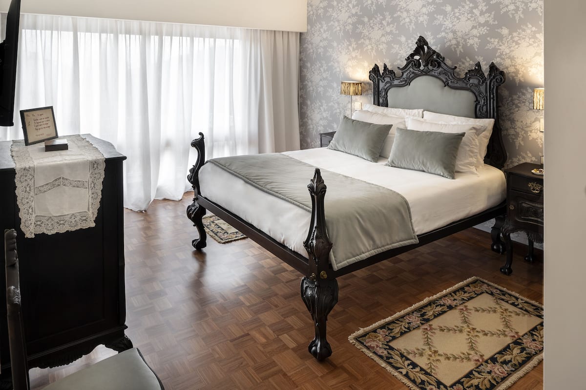 Een slaapkamer met een groot bed, een bureau met een lamp, een stoel en een raam met gordijnen.