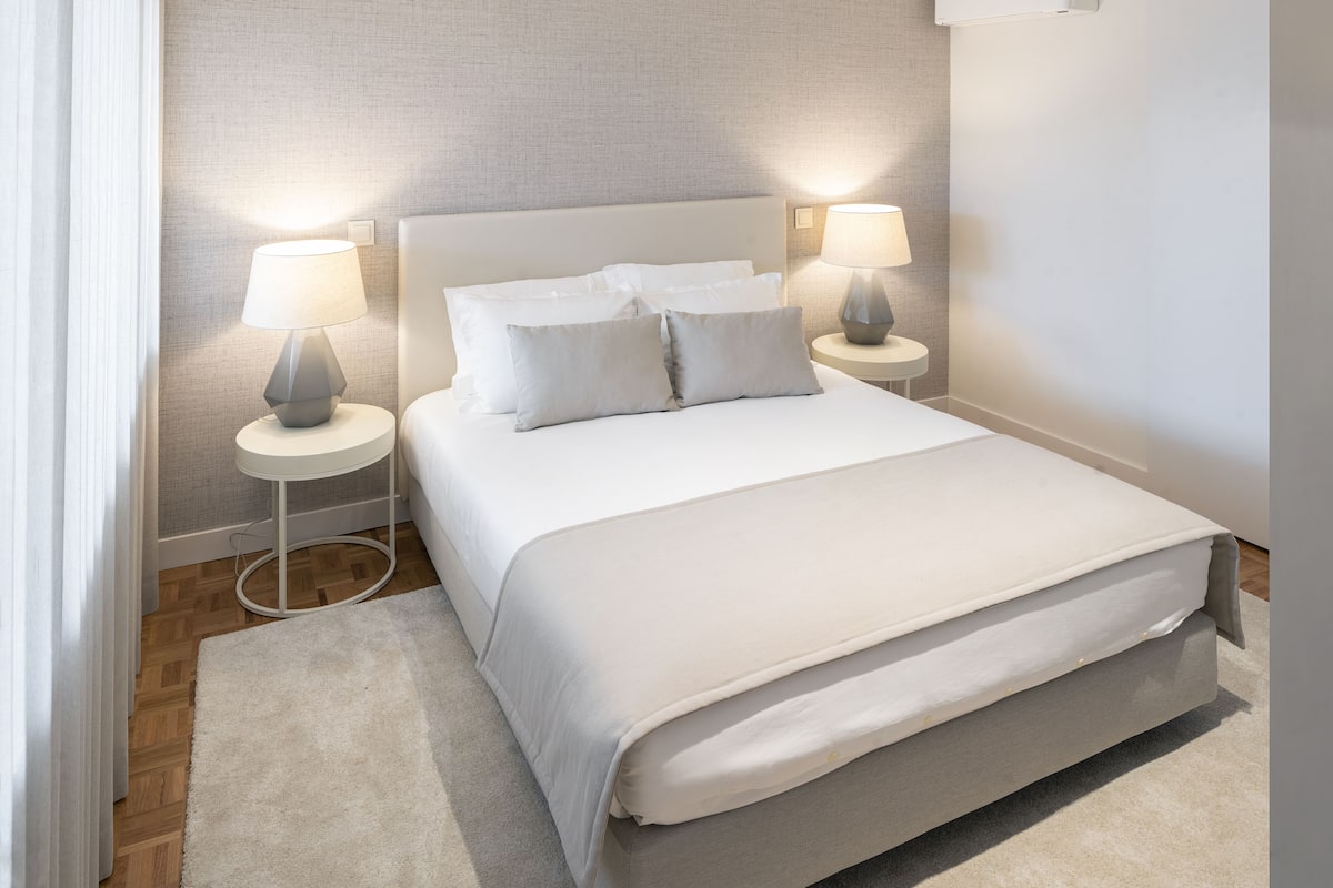 Een moderne slaapkamer met een groot bed, twee nachtkastjes met lampen, en een neutraal kleurenpalet.