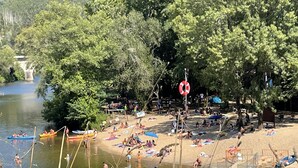 Een zandstrand aan de rivier met kano's, een reddingsboei en mensen die ontspannen op het zand en in het water.