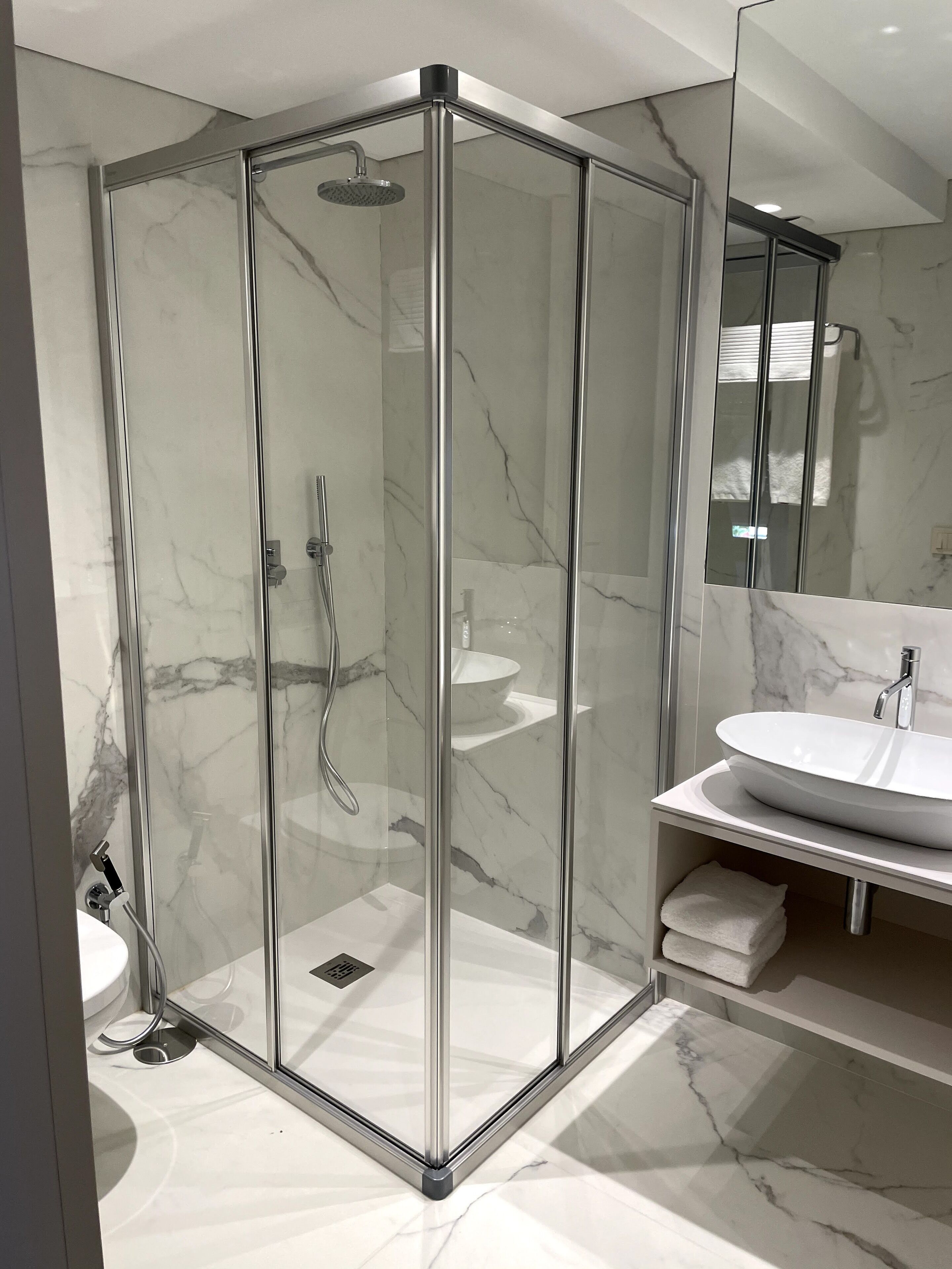 Een moderne badkamer met een douchecabine van glas, een wit wastafeltje en een marmeren vloer.