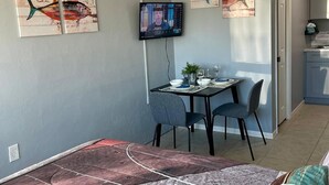 Un coin repas avec une table et des chaises, un téléviseur fixé au mur et des œuvres d’art représentant des poissons, accrochées aux murs.