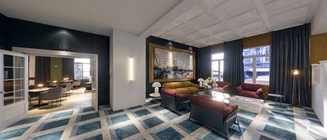 Eine moderne Hotelhalle mit einem geometrisch gemusterten Teppich, einem großen gerahmten Gemälde und einer Sitzecke mit einer Couch und Sesseln.