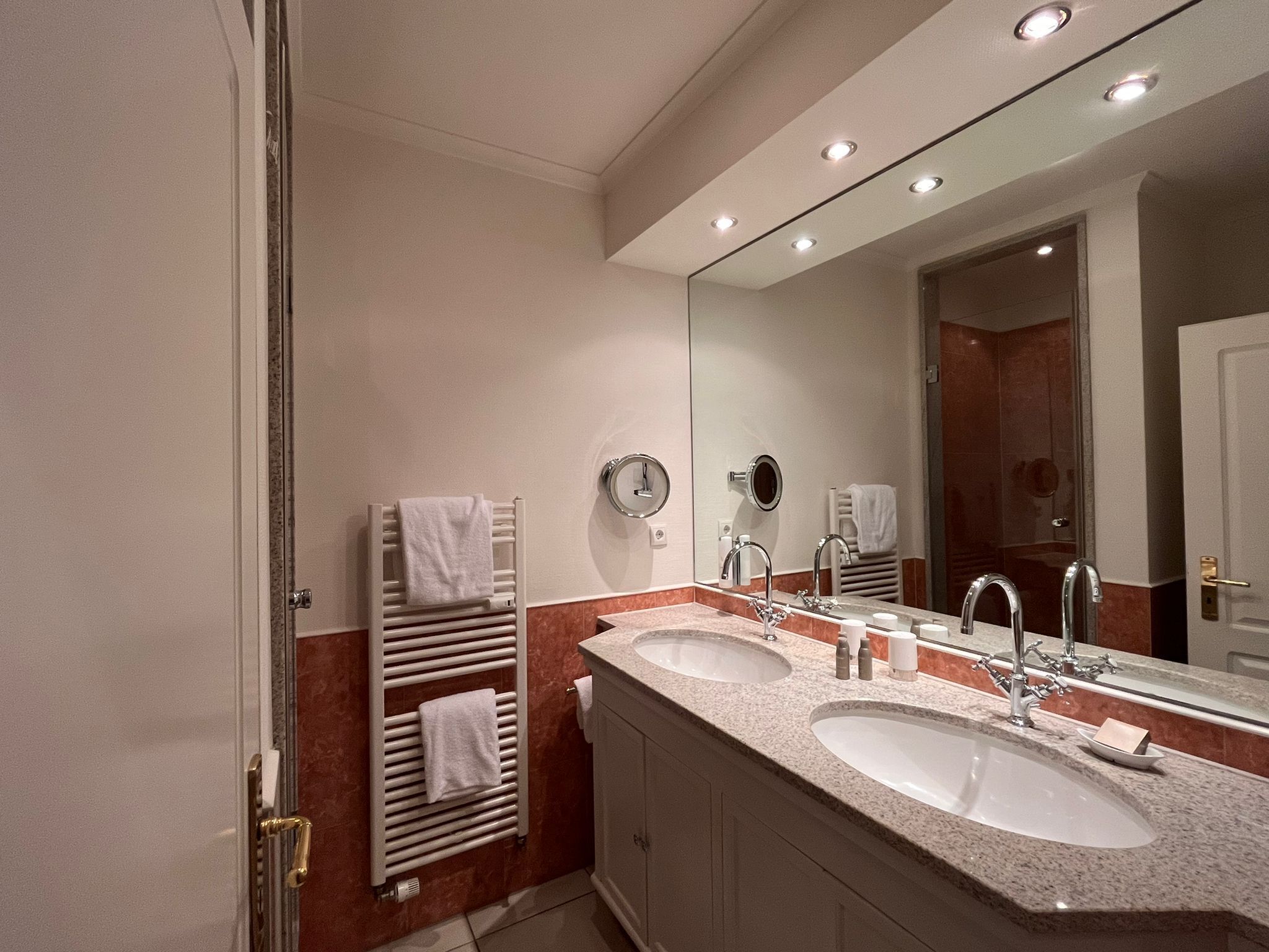 A modern bathroom with two sinks, a large mirror, and towel racks.