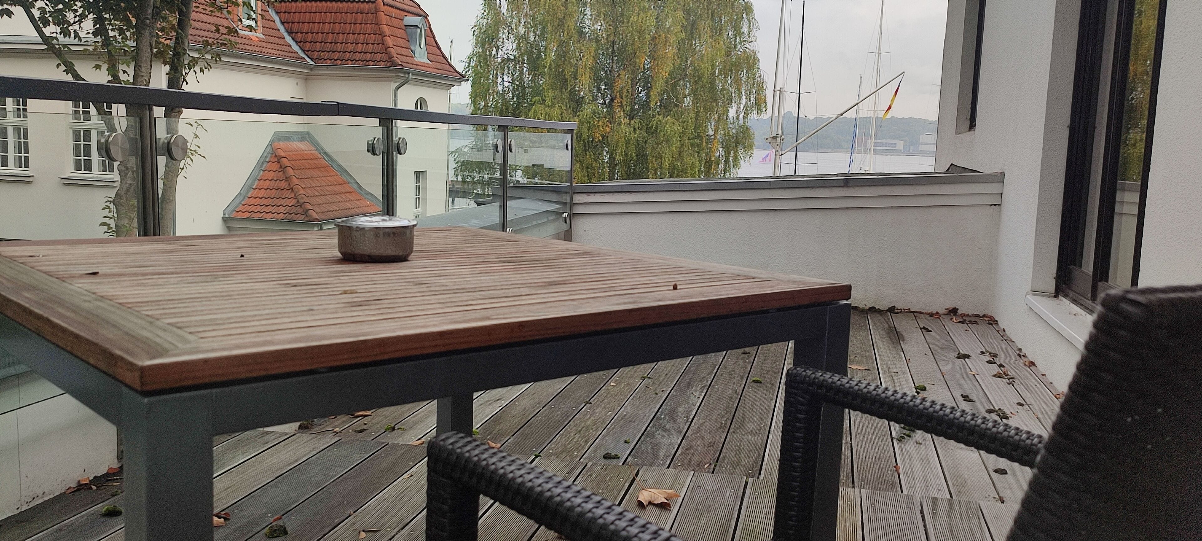 A balcony with a wooden table and a bowl, overlooking a cityscape with buildings and a river.