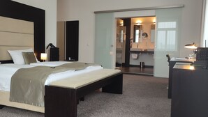 Habitació d'hotel moderna amb un llit gran, un escriptori i un bany visible a través d'una porta oberta.