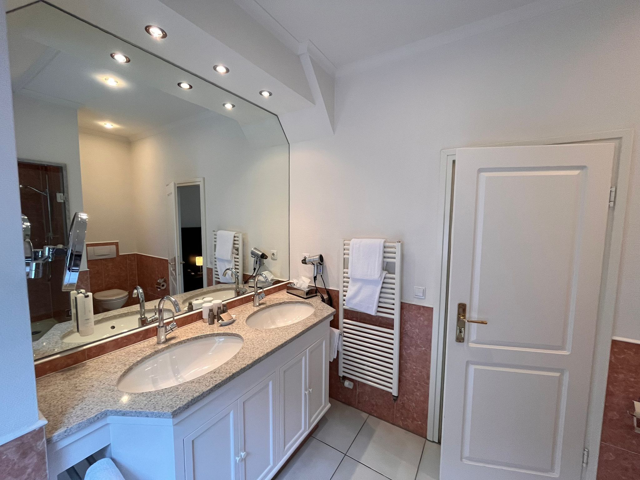 A modern bathroom with two sinks, a large mirror, and a towel rack.
