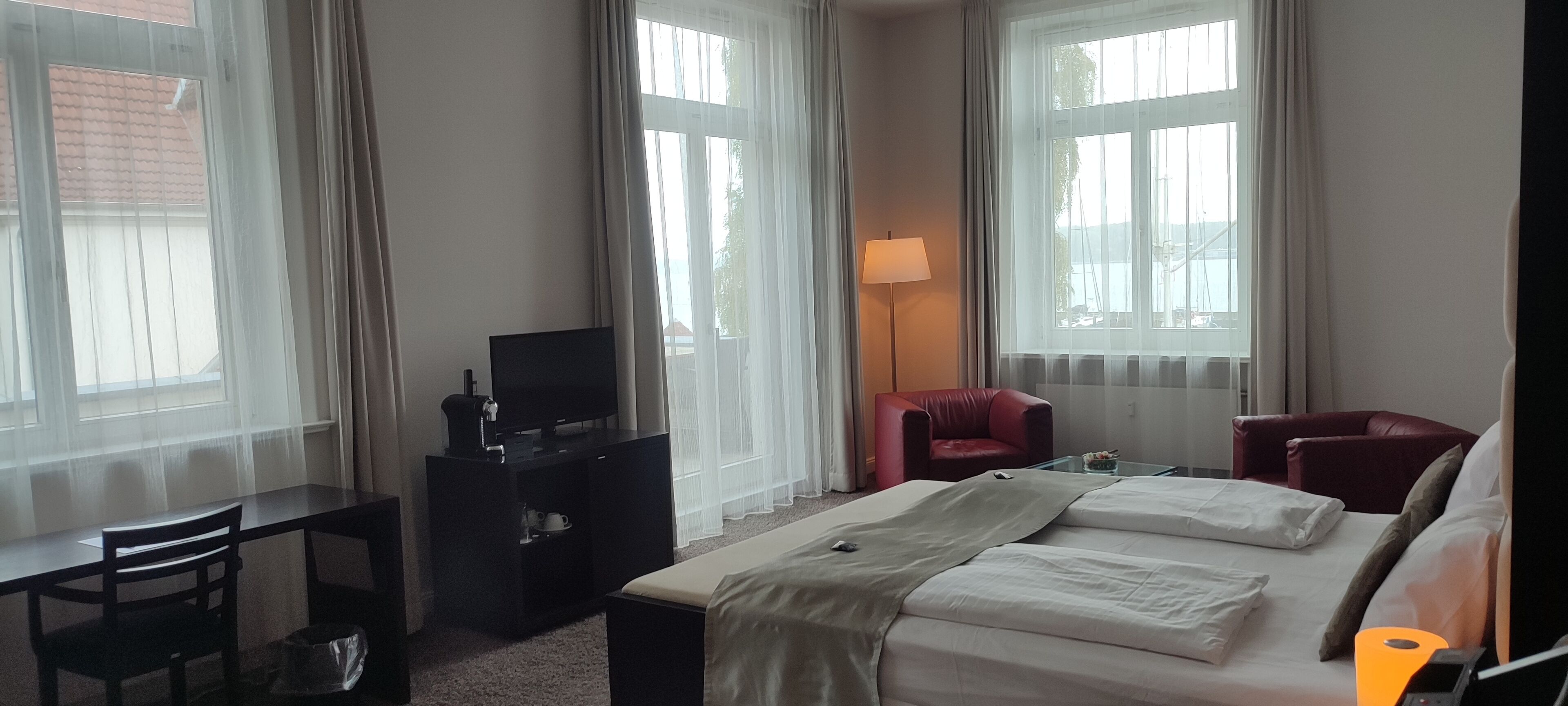 Een hotelkamer met een bed, een bureau, een televisie, een rode stoel en een lamp.
