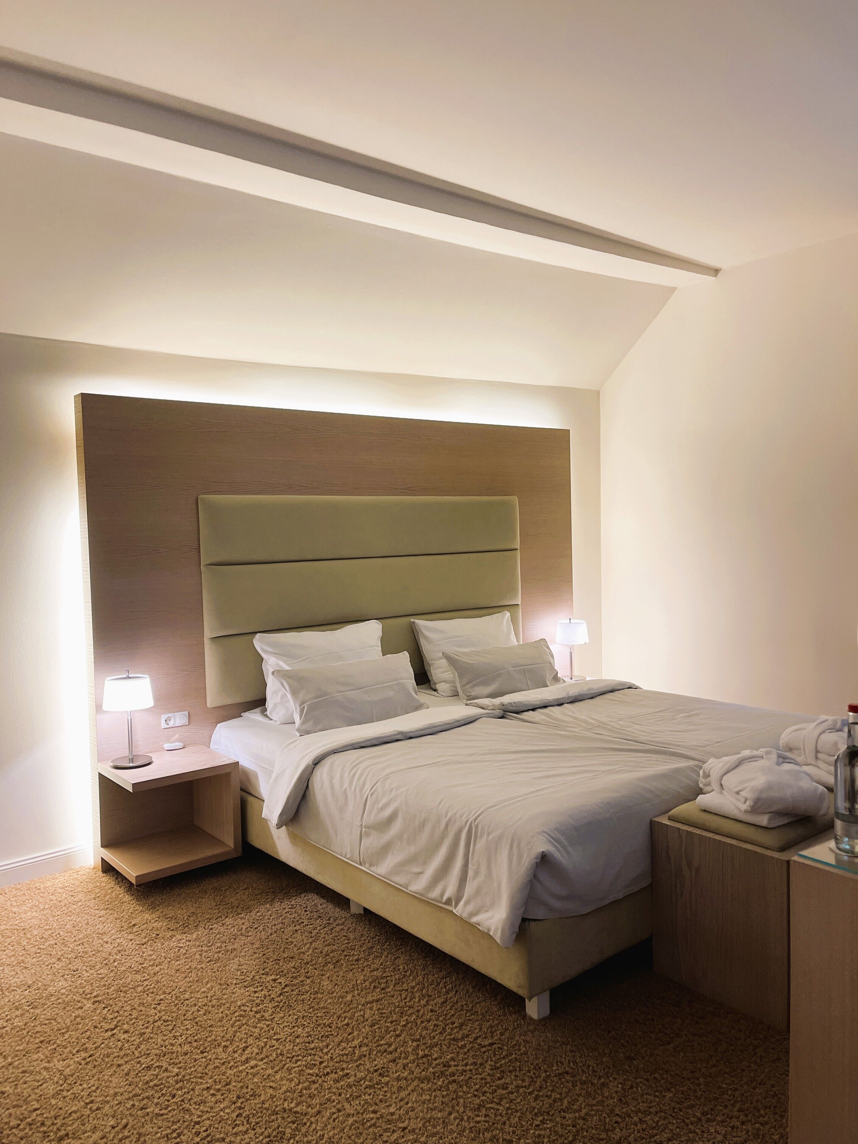 A neatly made bed with a headboard, two bedside tables with lamps, and a carpeted floor.