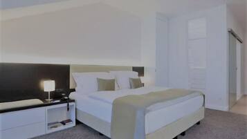A modern hotel room with a large bed, a bedside table with a lamp, and a wardrobe.