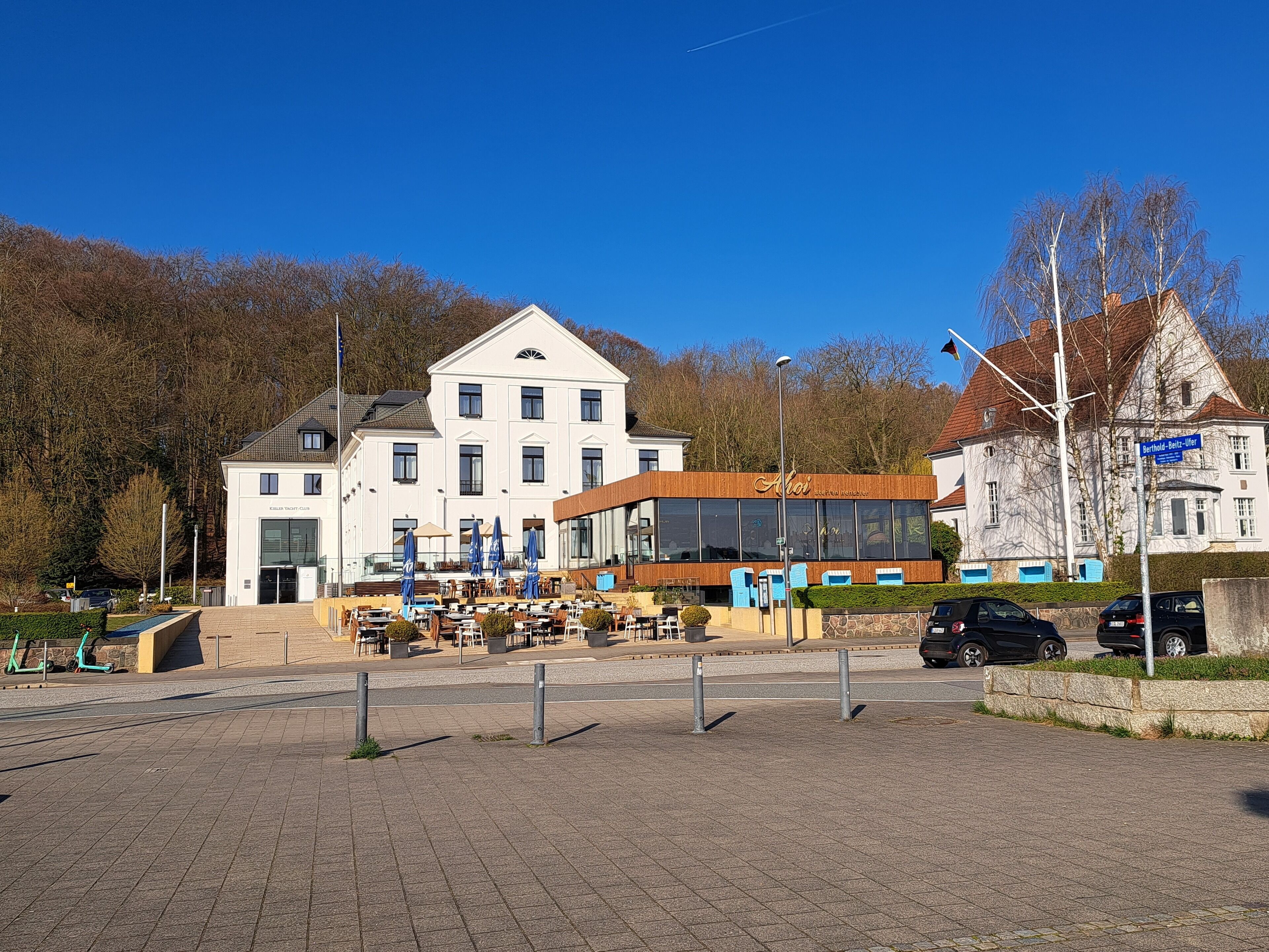 Un hotel con fachada blanca, zona de estar al aire libre y un edificio moderno con grandes ventanales.