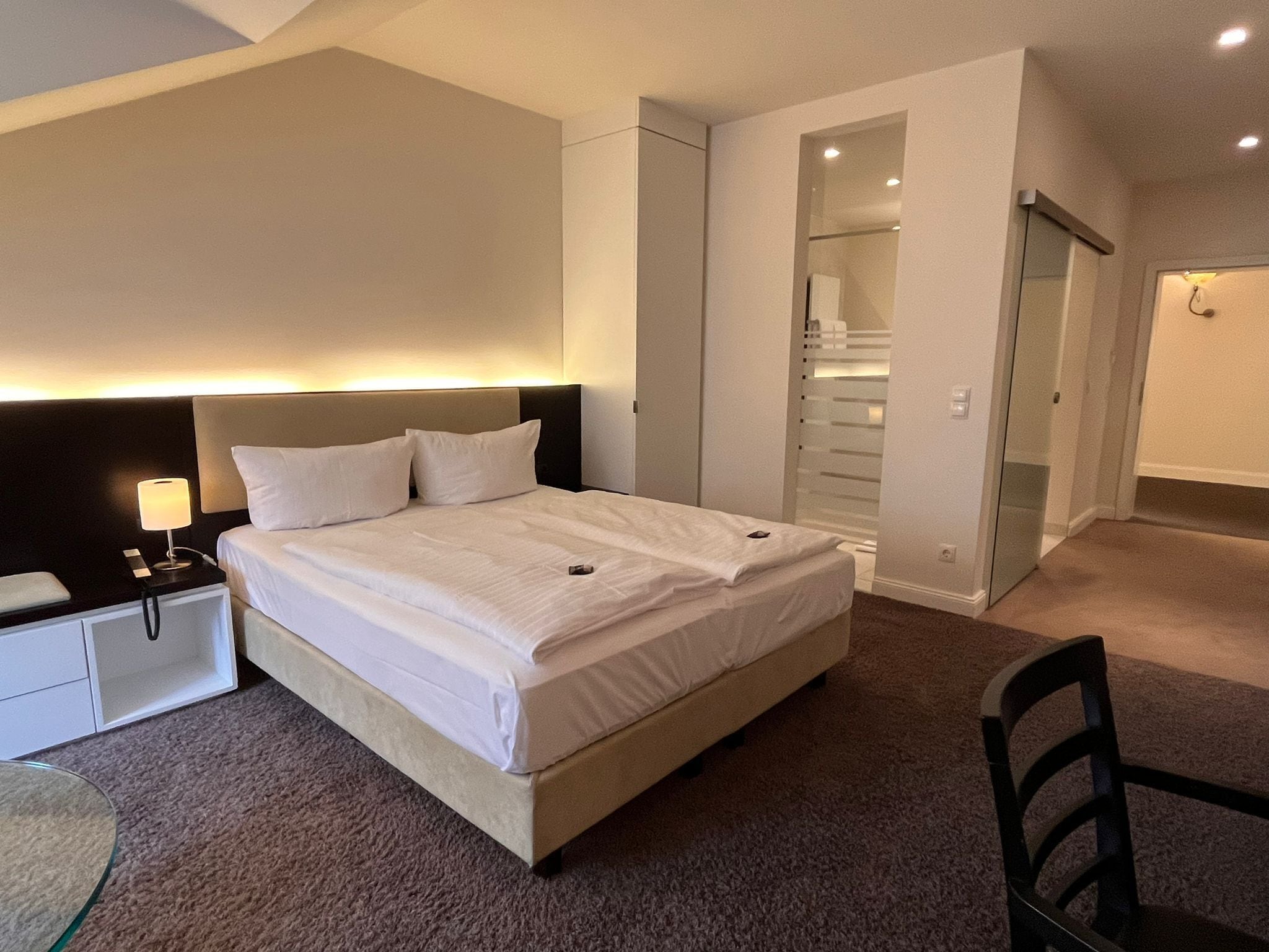 A hotel room with a bed, bedside table, lamp, and a chair.