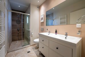 Un baño moderno con ducha de vidrio, lavamanos blanco y un espejo grande.