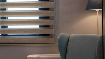 A room with a light blue armchair, a floor lamp, and horizontal blinds.
