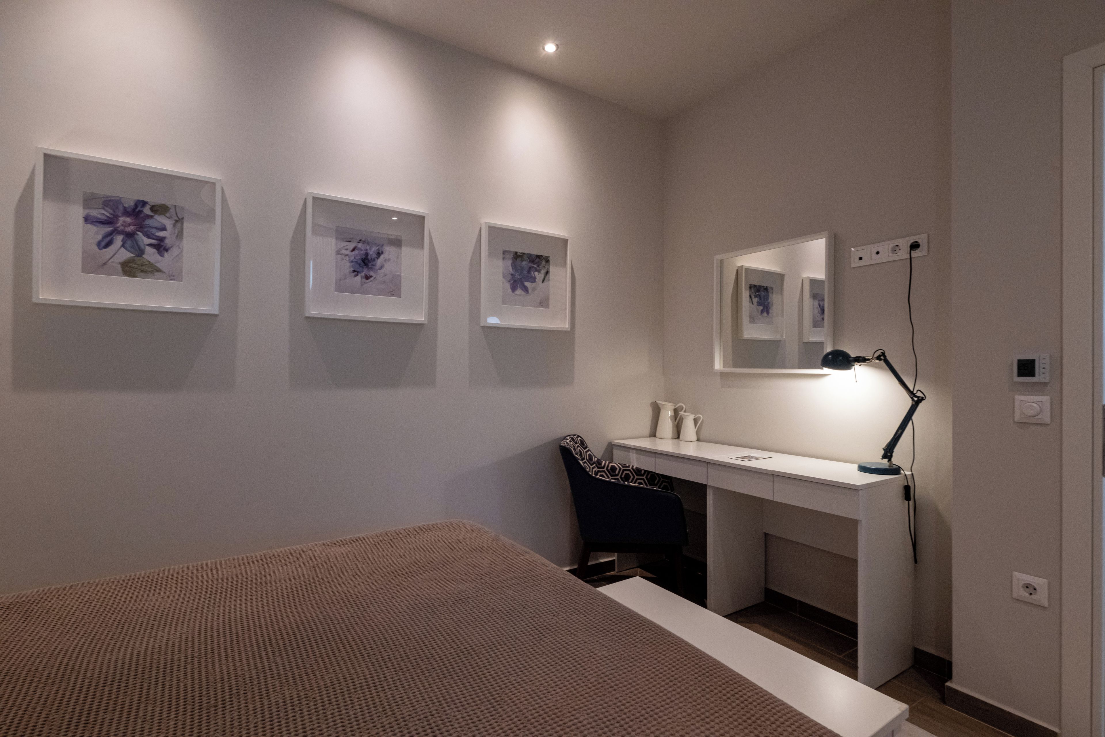 A bedroom with a bed, a desk, a chair, and three framed pictures on the wall.