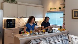 A modern kitchen with a built-in microwave, a dining area with a sofa, and a window with blinds. - Thalias Quarters - Kalamata Mediterranean Suites & Villas (Kalamata)