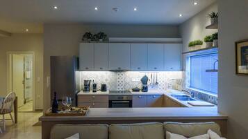 A modern kitchen with white cabinets, a central island, and a window with blinds.