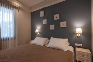 Una habitación de hotel con cama, dos mesitas de noche, aire acondicionado de pared y cuadros enmarcados.