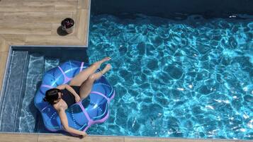 A person lying on a blue inflatable tube in a swimming pool with clear blue water.